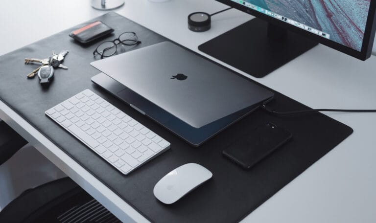 Un bureau avec un ordinateur portable Mac, une souris et un clavier offrant une prise en charge informatique.
